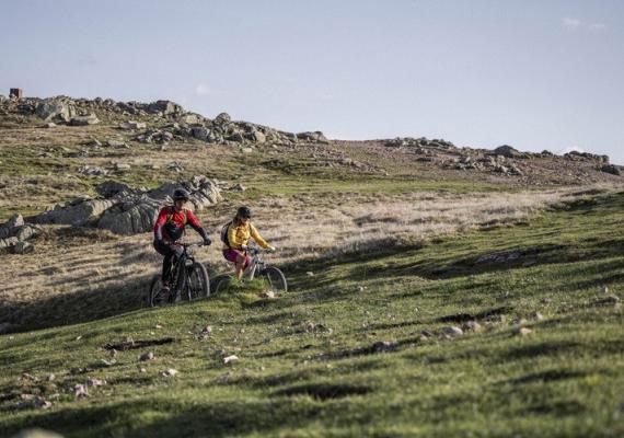 Two people riding bicycles on a green hill.