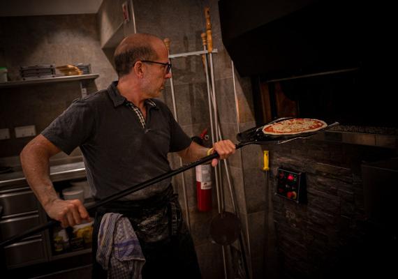 Un uomo tiene in mano un forno per pizza e una grande spatola di metallo nella pizzeria SchartnerAlm.