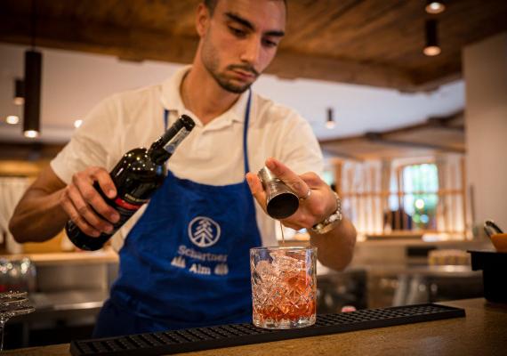 A man in a blue apron pours a drink in the SchartnerAlm pizzeria.