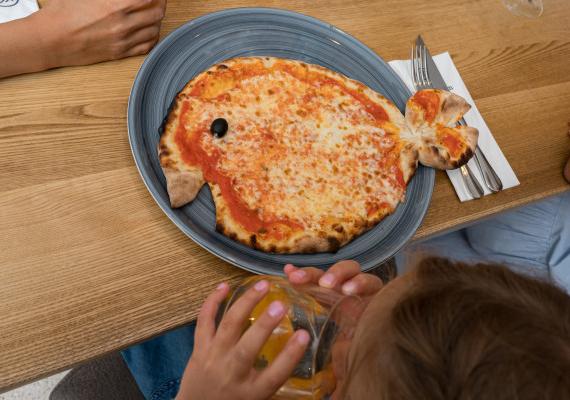 Ein Kind genießt eine Pizza in der Pizzeria SchartnerAlm